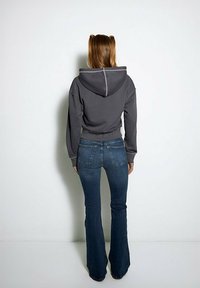 Beschnittenes graues Sweatshirt mit Kordelzug, kombiniert mit ausgestellten blauen Jeans. Hat einen gerippten Saum und seitliche Taschen.