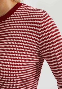 Pull en tricot rouge et blanc à motifs géométriques, encolure ronde et col côtelé, présentant un tissu texturé.