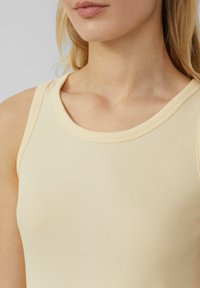 Geribbelde tanktop van zacht, lichtgeel materiaal met een ronde halslijn. Heeft een nauwsluitende pasvorm en minimale naden voor een schone uitstraling.