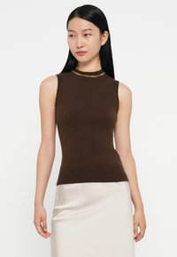 Bruine mouwloze top met een getailleerd ontwerp, geribbelde textuur en een gouden kettingaccent bij de halslijn; gedragen met een glanzende beige rok.