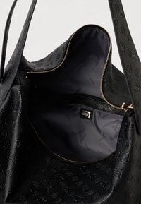 Saco tote preto texturizado com design de logotipo em relevo, fecho dourado e forro de tecido escuro com padrão de nome da marca repetido.