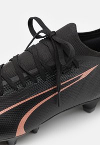 Scarpa da calcio nera con superficie texturizzata, dotata di accenti diagonali rosa, lacci tondi e tacchetti stampati per la trazione.