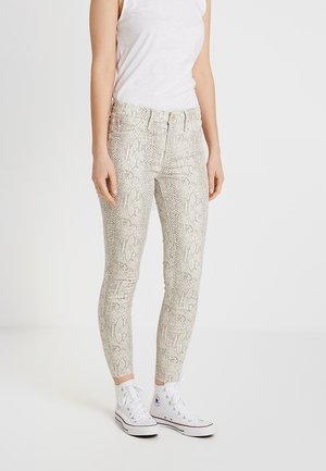 Jeans skinny con stampa serpente in beige chiaro con finitura lucida, dotati di vita media e cinque tasche. Abbinati a sneakers alte bianche.