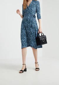 Sukienka w kwiaty w kolorze granatowym z małymi niebieskimi i białymi kwiatkami. Para czarnych sandałów na słupku i czarna torebka z okrągłym detalem metalowym.