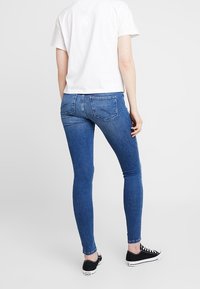 Tunna blå denimjeans med medelhög midja, bakfickor och en mjuk textur, i kombination med en vit t-shirt med kort ärm och svarta sneakers.