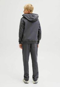 Felpa con cappuccio grigia in misto cotone, con tasca a marsupio e polsini a coste, abbinata a pantaloni della tuta coordinati e sneakers.
