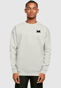 Sudadera gris claro hecha de tela suave, con un diseño de gato negro en el lado izquierdo del pecho. Cuello redondo clásico y puños acanalados.