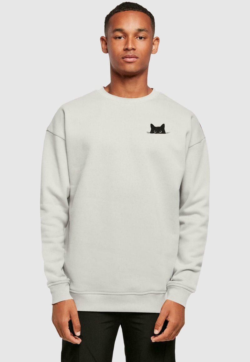 Sudadera gris claro hecha de tela suave, con un diseño de gato negro en el lado izquierdo del pecho. Cuello redondo clásico y puños acanalados.