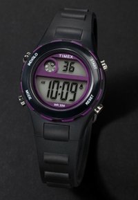 Zegarek cyfrowy Timex z czarnym gumowym paskiem i fioletowymi detalami. Posiada prostokątną tarczę, wyświetlacz LCD oraz liczne przyciski do obsługi funkcji.