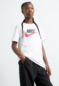 White cotton t-shirt featuring a black and red Nike logo, paired with black pants that have a zippered pocket. Simple crew neck design.