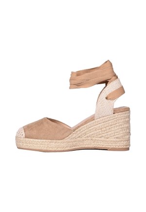 Sandalo espadrillas beige con zeppa, punta chiusa, suola in corda e cinturino da annodare alla caviglia su sfondo bianco.