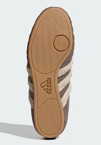 Brown sneaker sole featuring a textured gum rubber outsole, suede upper with cream stripes, and an Adidas logo embossed near the heel.