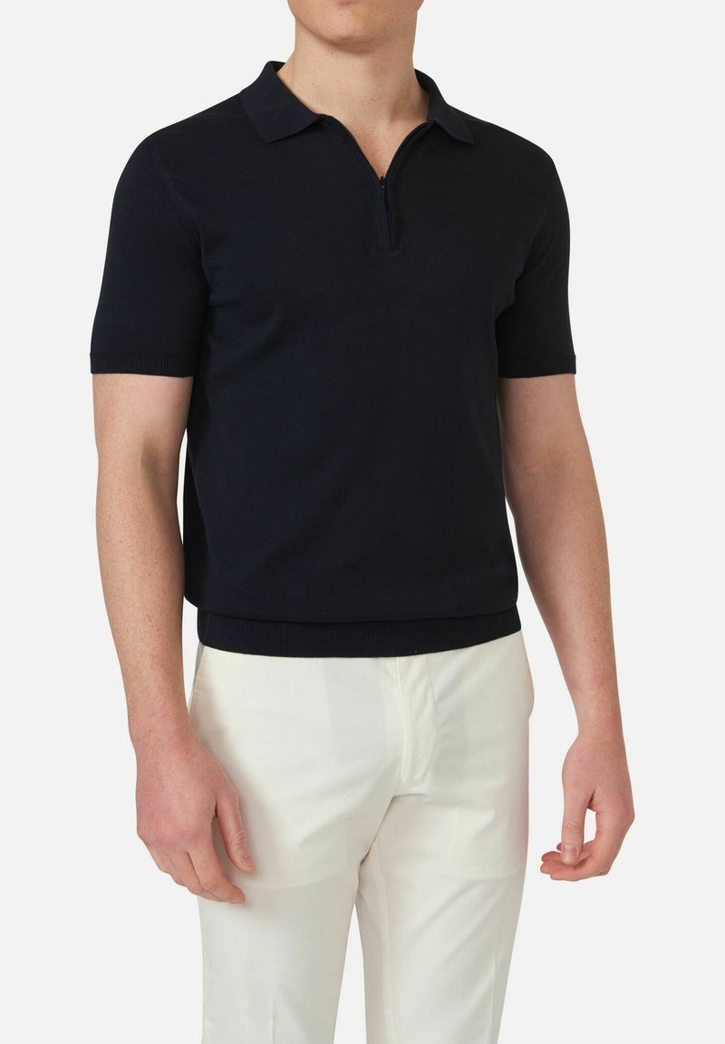 Navy short-sleeve polo shirt made of knit fabric, featuring a half zip collar and ribbed cuffs and hem, paired with white pants.