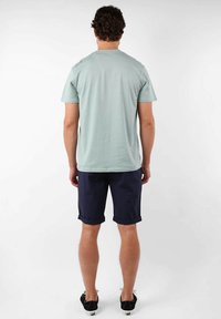 T-shirt en coton vert clair à manches courtes, associé à un short bleu marine retroussé. Le dos présente un design minimal et aucune graphique visible.