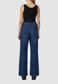 Jean en denim taille haute, à jambes larges, de couleur bleu foncé. Comprend deux poches arrière, des coutures contrastées et une fermeture à bouton à la taille.