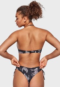Conjunto de bikini negro con un diseño estampado con motivos de leopardo blancos. La parte superior tiene un cierre en la espalda y tirantes finos; la parte inferior tiene lazos ajustables.