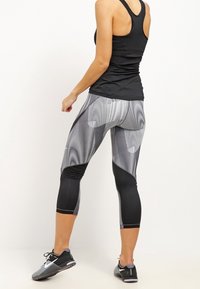 Top negro de tirantes combinado con leggings capri en negro y gris con estampados que presentan texturas variadas y diseños geométricos. Calzado en negro con detalles en blanco.