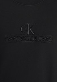 Černá mikina s výšivkou "CK" a značkou "CALVIN KLEIN JEANS". Hladký materiál s žebrovaným výstřihem.