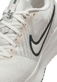 Zapatilla de correr Nike blanca con parte superior de malla texturizada, logo swoosh negro y cordones blancos. Cuenta con una suela acolchada para mayor soporte.