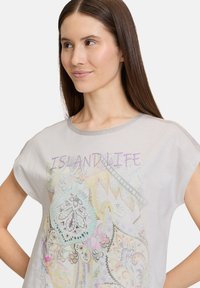 Lichtgrijs T-shirt met korte mouwen met kleurrijke paisleyprint en de tekst "ISLANDLIFE" in paars, met metallic zilveren afwerking.