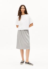 White cropped t-shirt with pink accent detail, paired with a gray elastic waistband midi skirt. Model wears black sneakers.