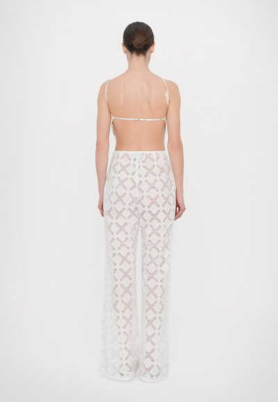 Witte, ontworpen wijde broeken met een geometrisch patroon, met een hoge taille en doorzichtige textuur. Het achteraanzicht benadrukt de open rug en dunne bandjes.