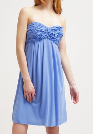 Robe bleu clair sans bretelles avec corsage froncé et ornements floraux sur la poitrine portée par une personne à la peau claire et aux cheveux roux.