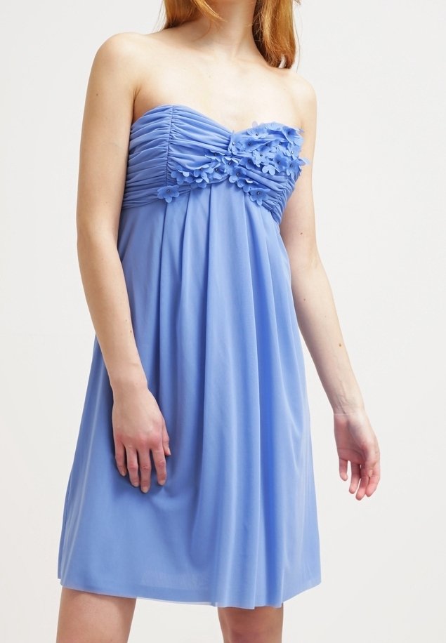 Robe bleu clair sans bretelles avec corsage froncé et ornements floraux sur la poitrine portée par une personne à la peau claire et aux cheveux roux.