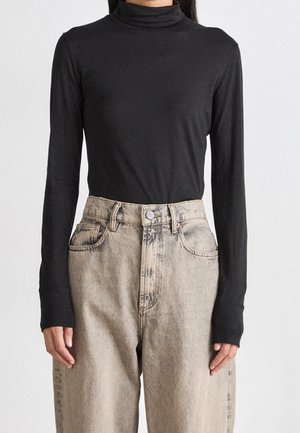 Kobieta ubrana w dopasowany czarny golf z długim rękawem, wsadzony w jasne, luźne jeansy z wysokim stanem.