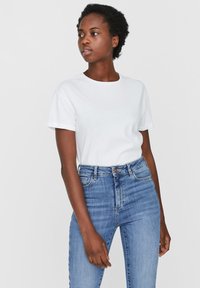 Witte katoenen t-shirt met korte mouwen en een ronde halslijn, gecombineerd met hoog-waist blauwe jeans, weergegeven tegen een neutrale achtergrond.