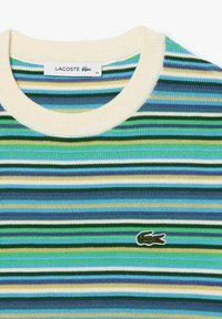 Stribet striktrøje i grønne, blå og gule nuancer med ribbet cremegul halsudskæring. Lacoste-logoet er broderet på brystet.
