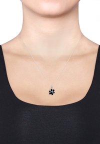 Silversmyckad kedja med en svart tassavtryckpendel, som visar en slät yta och en detaljerad tassdesign.
