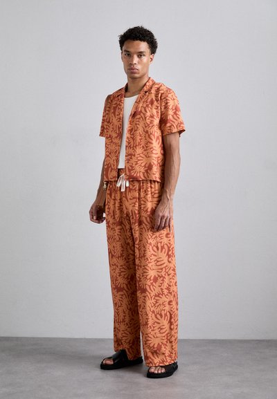 Short-sleeved, collared shirt and matching loose pants in orange with beige abstract floral pattern. Fabric appears lightweight and soft.