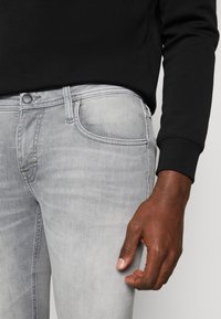 Ljust grå jeans med en slim fit-design, med klassisk fem fickor-stil, metallknapp och subtil blekning längs benet.
