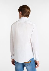 Hvid langærmet skjorte med klassisk krave, knaplukning ved håndleddene, blød tekstur og glat finish. Kombineret med blå jeans.