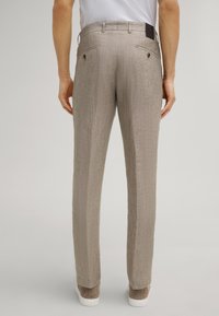 Beige gemusterde broek van een textuurstof, met achterzakken en een label op de tailleband. Een rechte snit en subtiele ontwerpdetails.
