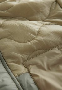 Gequilte dekbed in een beige tint, met een zachte textuur en een subtiel ruitpatroon en gestikte accenten. Inclusief een grijze rand.