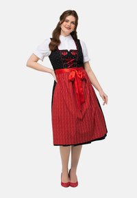 Traditioneel kostuum met een zwarte corsage versierd met bloemembroidery, een rode rok met verticale patronen en een rode strik vastgebonden rond de taille.