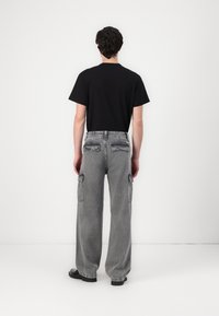 Black short-sleeve t-shirt paired with gray denim cargo pants featuring multiple pockets, a relaxed fit, and visible stitching details.