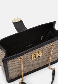 Beige käsilaukku, jossa on geometrinen kuvio, mustat nahkanyörit, kultaiset yksityiskohdat, ketjuhihna ja vetoketjullinen sisätasku.