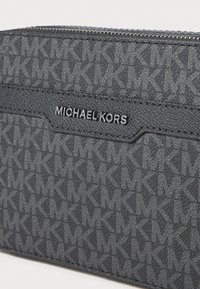 Michael Kors pilkas audinys su tekstūru ir logotipo raštu, su sidabro logotipo plokšte ir užtrauktuku viršuje.