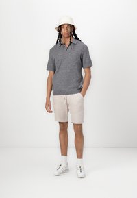 Šedé textúrované polo tričko s krátkym rukávom, béžové kraťasy s šnúrkou, biele sneakers a svetlý klobúk. Jednoduchý a neformálny outfit.