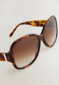 Übergroße Sonnenbrille in Schildpatt-Optik mit großen braunen Verlaufsgläsern und einem dezenten goldenen Akzent am Rahmenbügel.