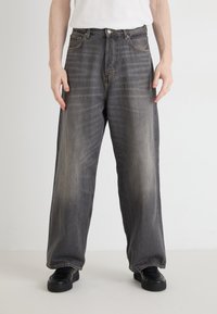 Jean en denim noir délavé à jambes larges. Présente un design classique à cinq poches, une fermeture à bouton en métal et un léger effet d'usure sur le tissu.