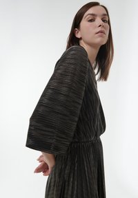 Robe noire plissée avec des rayures métalliques, dotée de manches larges et d'une taille cintrée. Texture lisse avec un léger éclat.