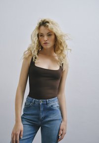 Top in tessuto marrone attillato con scollo quadrato abbinato a jeans in denim blu a vita alta. Il tessuto è morbido e la silhouette complessiva è elegante.