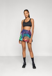 Soutien-gorge de sport noir, jupe colorée à motifs géométriques, longueur mi-cuisse, associée à des chaussures de sport et des chaussettes noires.