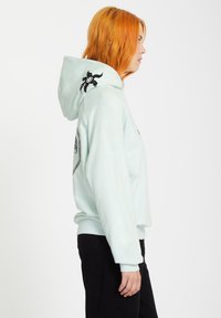 Mintgrön hoodie med framficka, svarta grafiska detaljer, ribbade muddar och avslut. Mjuk textur, avslappnad design och en ledig passform.