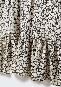 Tela con estampado floral en negro y crema, que presenta un dobladillo con volantes y una textura estriada, con motivos florales dispersos por toda la superficie.