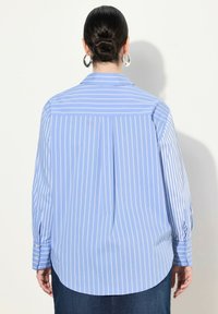 Camicia button-up azzurro chiaro con strisce bianche verticali, maniche lunghe, tessuto morbido e vestibilità rilassata, con una piega sul retro e orlo arrotondato.